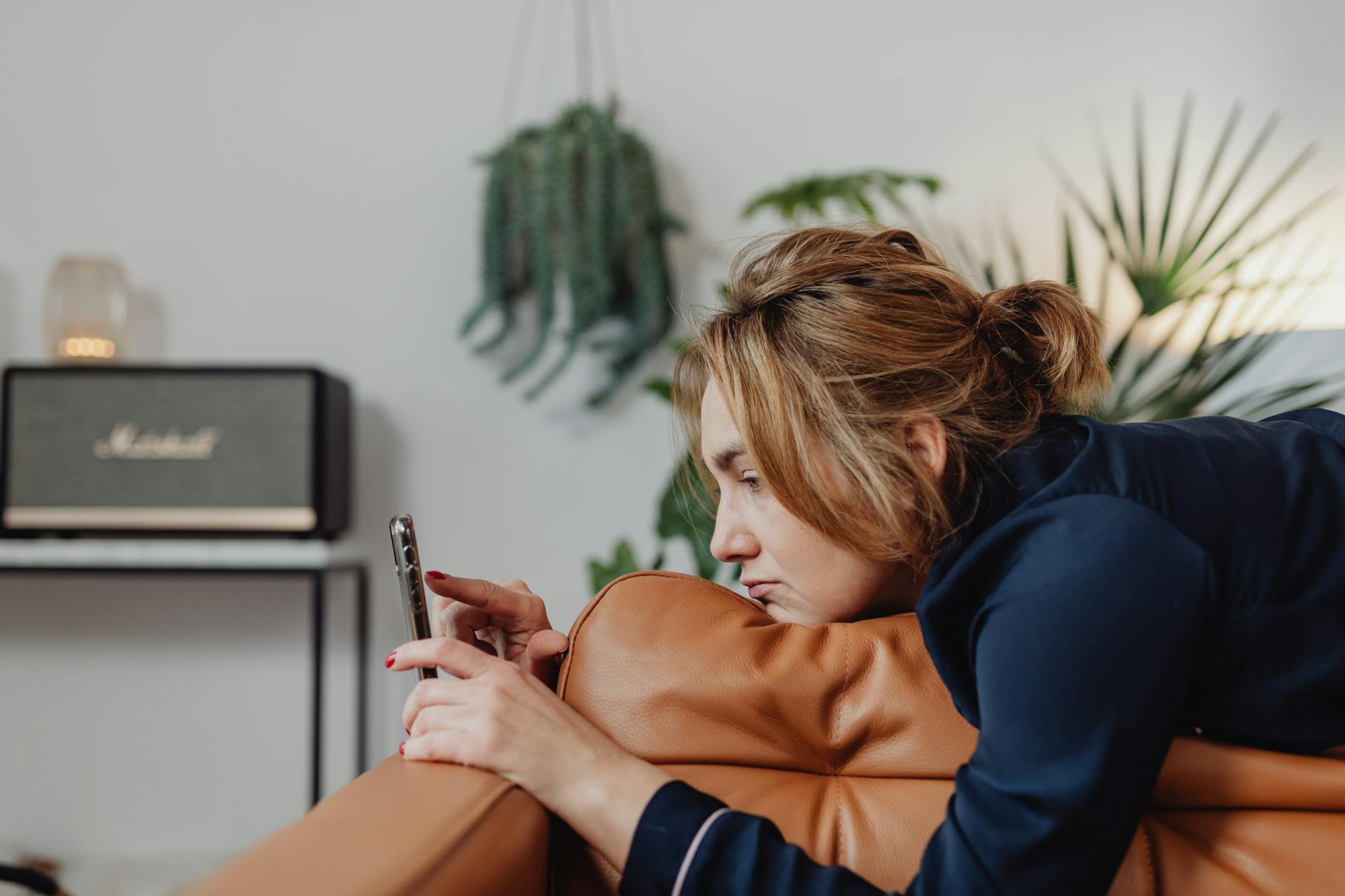 woman with messy hair lying down on a couch using her cellphone